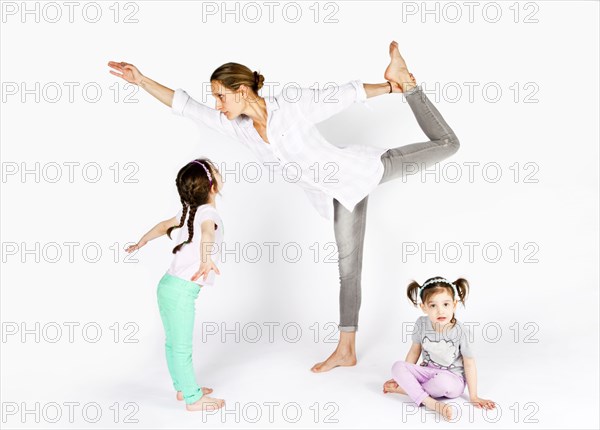 Mother practicing yoga with playful daughters