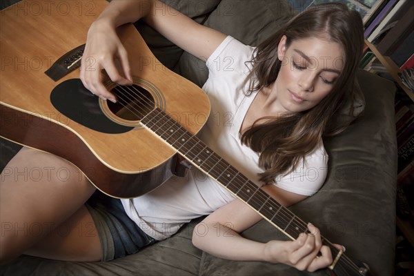 Caucasian woman playing guitar on sofa