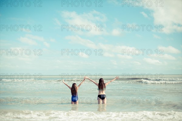 Caucasian sisters standing in waves on beach