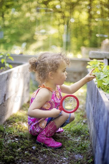 Girl examining garden plants with magnifying glass