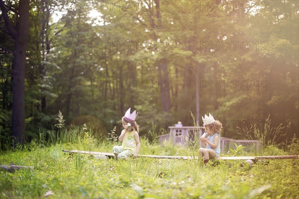 Girls playing telephone on wooden log in garden