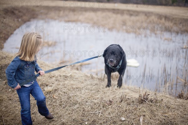 Girl pulling dog on leash near rural pond