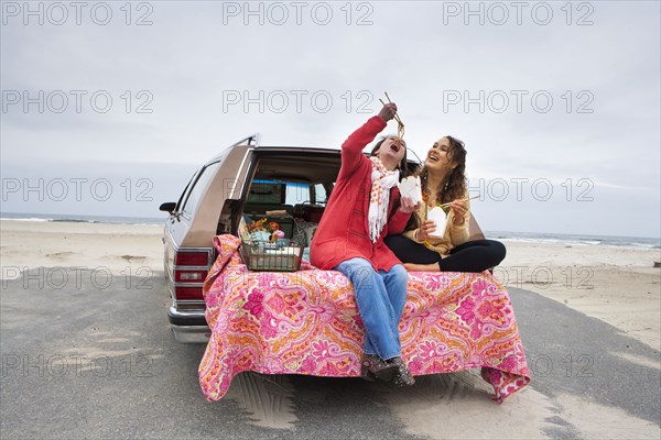 Caucasian mother and daughter eating noodles in car trunk on beach