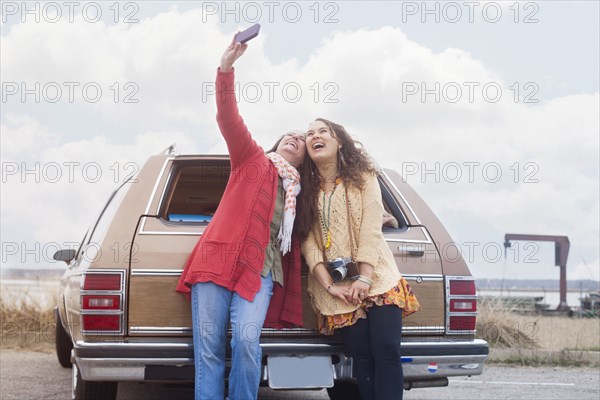 Caucasian mother and daughter taking selfie near car