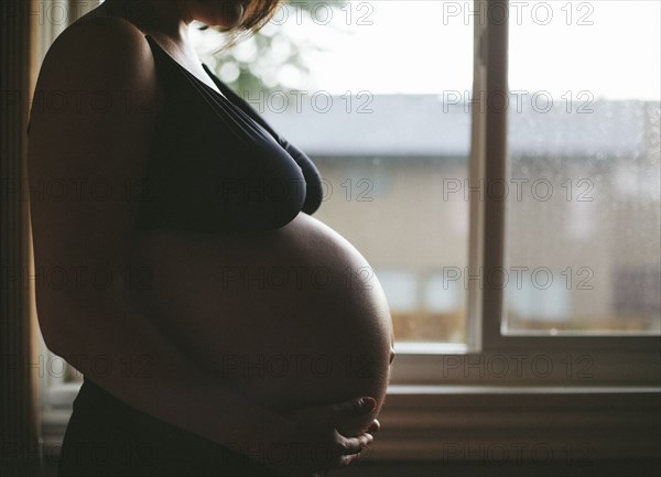 Pregnant Caucasian woman standing at window