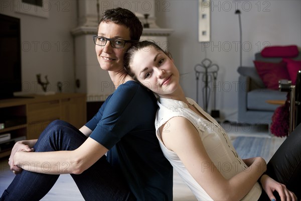 Caucasian mother and daughter sitting back to back