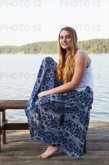 Caucasian teenage girl sitting on wooden dock at lake
