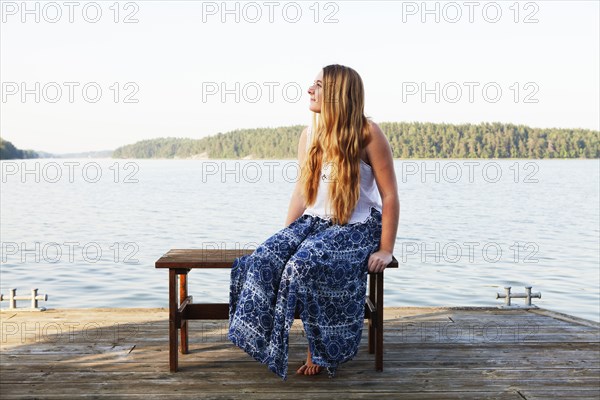 Caucasian teenage girl sitting on wooden dock at lake