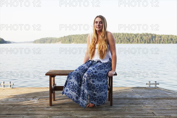 Caucasian teenage girl sitting on wooden dock at lake