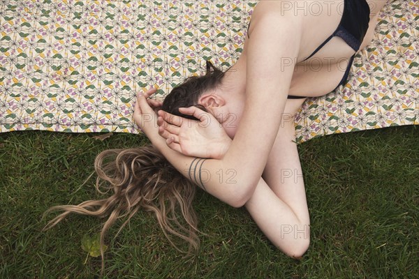 Woman sunbathing in bikini on blanket in grass