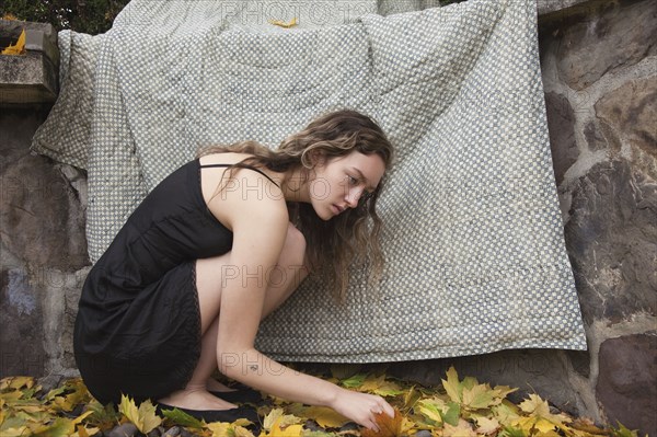 Woman crouching under blanket near stone wall