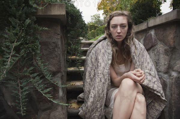 Woman wrapped in blanket sitting on stone steps