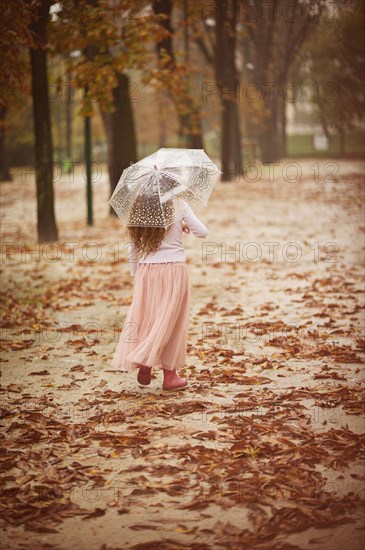 Caucasian girl carrying umbrella in park