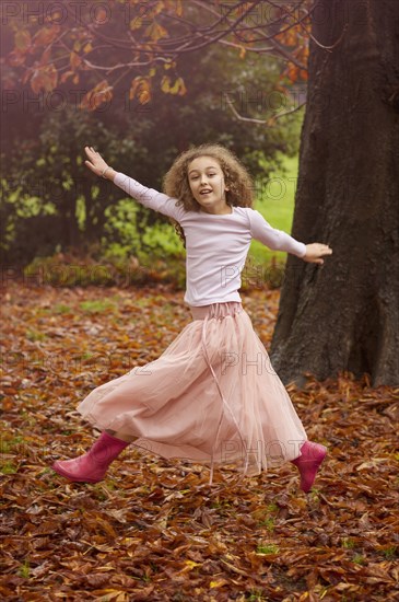 Caucasian girl jumping for joy in autumn leaves