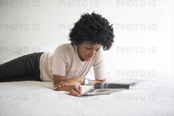 Black woman reading magazine on bed