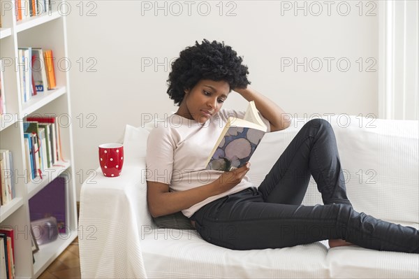 Black woman reading book on sofa