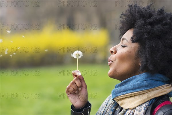 Black woman blowing dandelion seeds in park