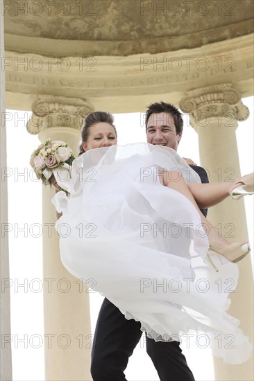 Caucasian groom carrying bride after wedding