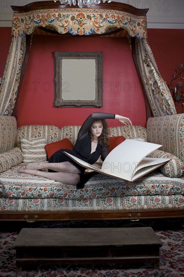 Woman reading oversized book on sofa in ornate living room