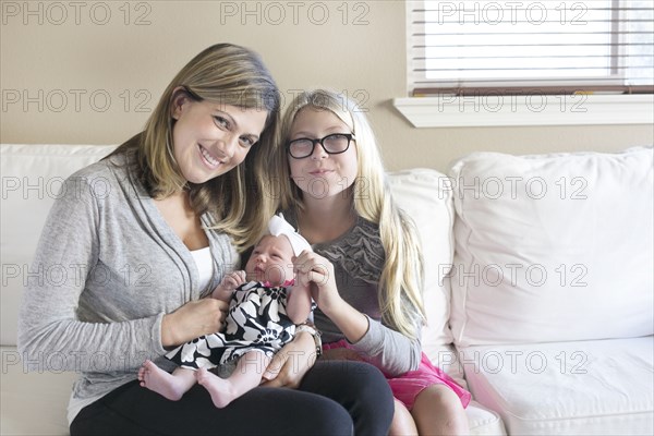 Caucasian mother and daughter cuddling newborn on sofa