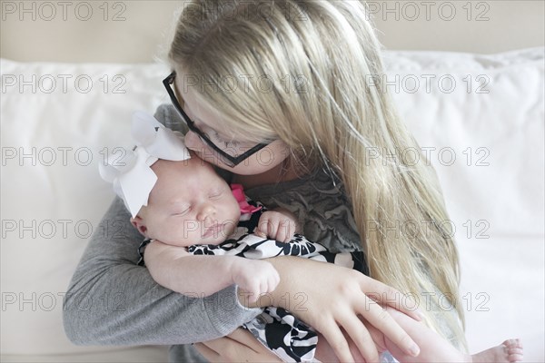 Caucasian girl kissing newborn sister on sofa