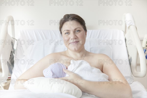 Caucasian mother nursing newborn daughter in hospital bed