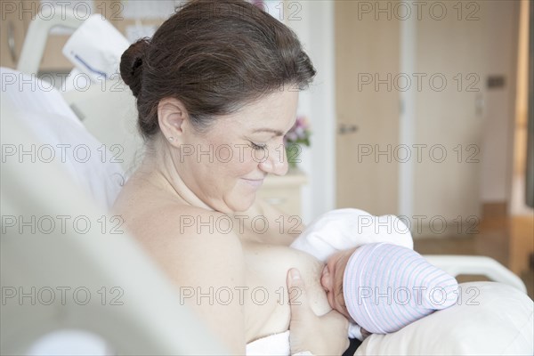 Caucasian mother nursing newborn daughter in hospital bed