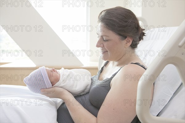 Caucasian mother holding newborn daughter in hospital bed