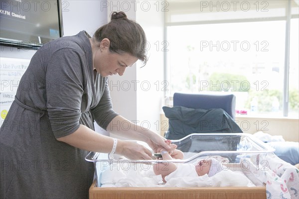 Caucasian mother changing newborn daughter in hospital crib