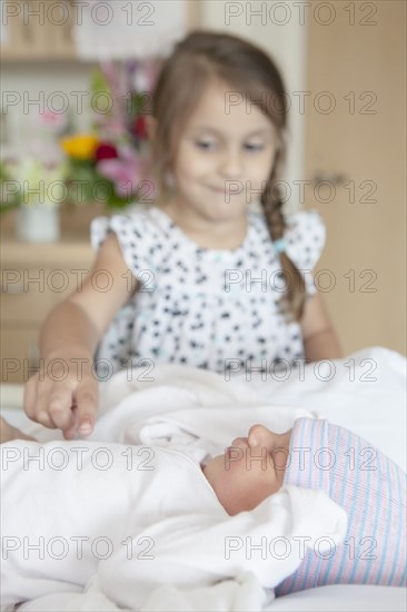 Girl admiring newborn sister on hospital bed