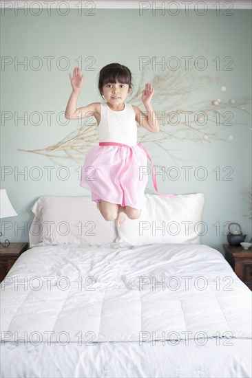 Hispanic girl jumping on bed