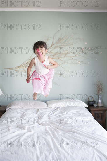 Hispanic girl jumping on bed