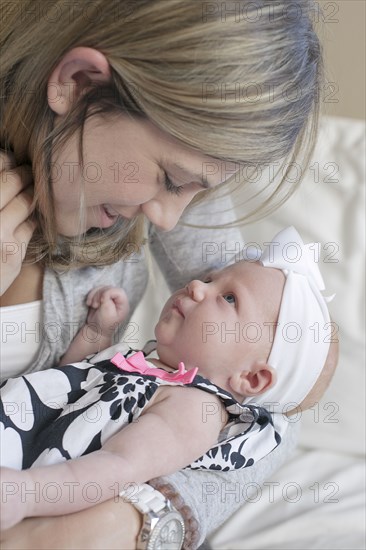 Caucasian mother kissing newborn daughter on sofa