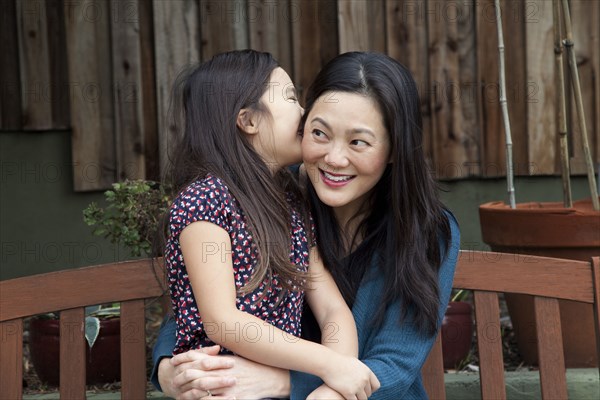 Mother and daughter whispering secrets in backyard