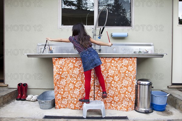 Mixed race girl cleaning paintbrushes in sink