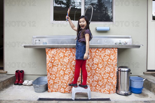 Mixed race girl showing clean paintbrushes at sink