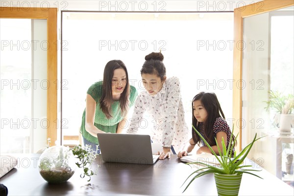 Mother and daughters using laptop in dining room