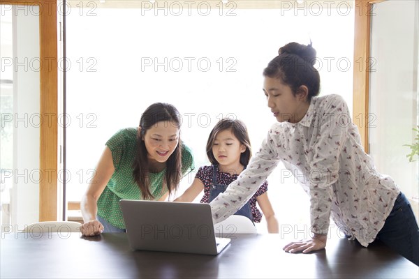 Mother and daughters using laptop in dining room