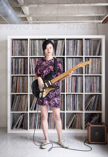 Taiwanese woman playing electric guitar near record collection