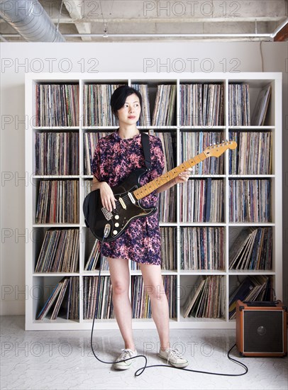 Taiwanese woman playing electric guitar near record collection