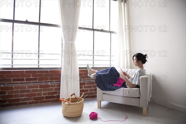 Taiwanese woman knitting in armchair near window