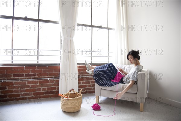 Taiwanese woman knitting in armchair near window