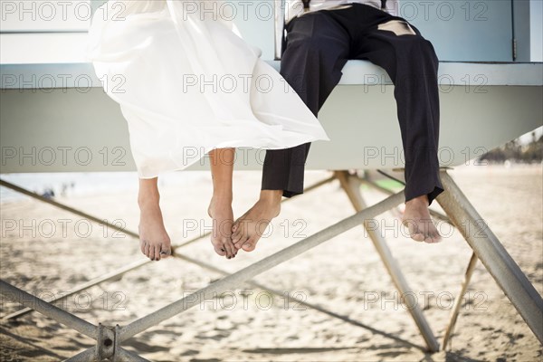Asian bride and groom sitting on lifeguard hut on beach