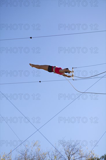 Acrobat hanging from trapeze under blue sky