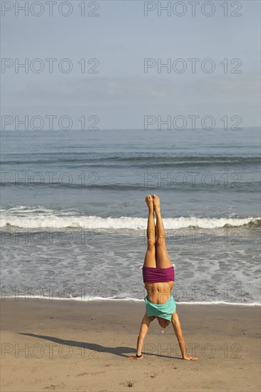 Caucasian woman doing handstand on beach