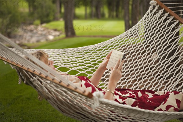 Woman reading book in backyard hammock