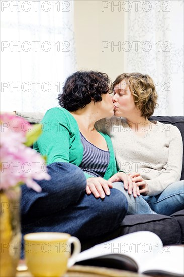 Lesbian couple kissing on sofa in living room