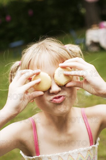 Close up of girl holding cookies over eyes in backyard
