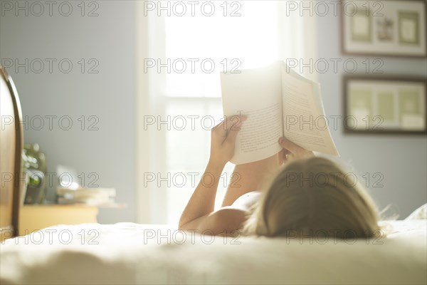 Caucasian girl reading book on bed