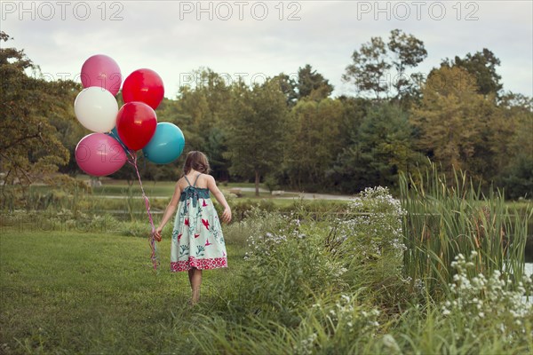 Caucasian girl carrying balloons in rural field